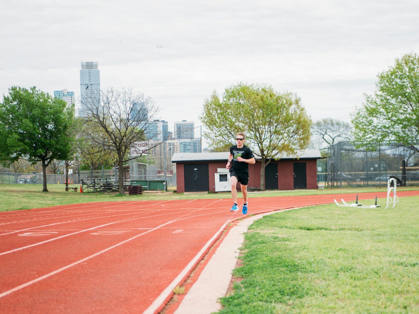 An athlete in black sportswear runs on an outdoor track.